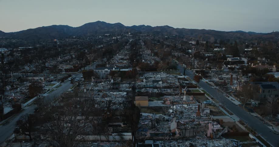 Aerial view shows the devastating aftermath of a fire in a residential area with mountains in the distance