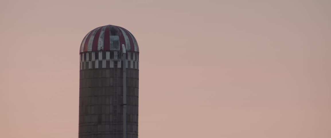A tall silo with a red and white striped dome stands prominently against the sunrise sky