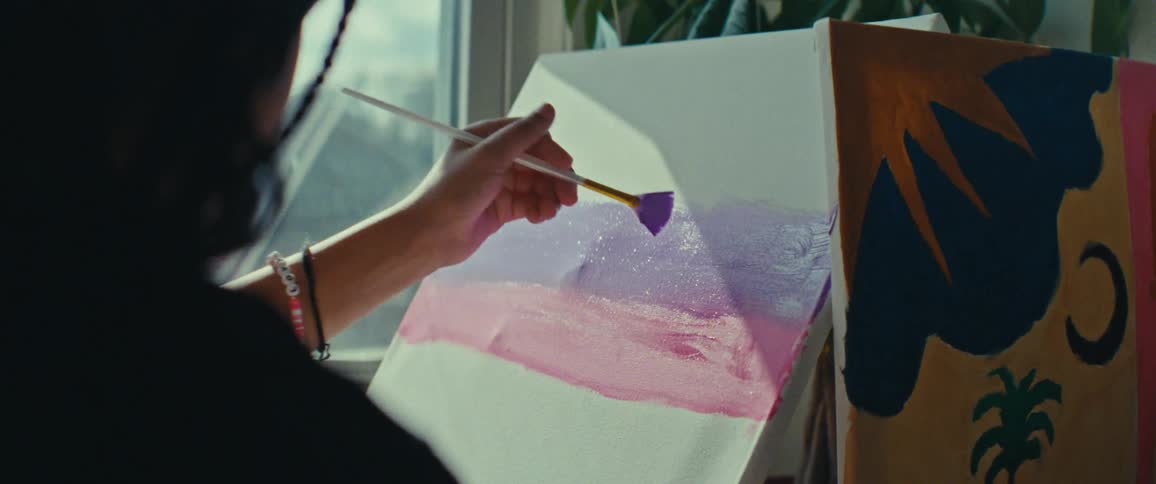 A person is painting on a canvas using a brush creating a gradient of pink and purple colors