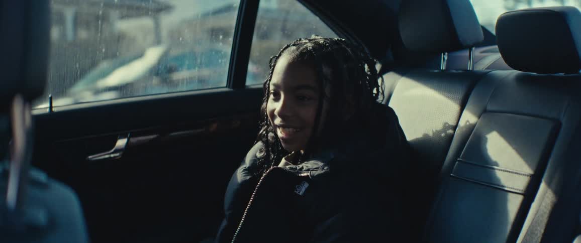 A child smiles and raises her arms in the car