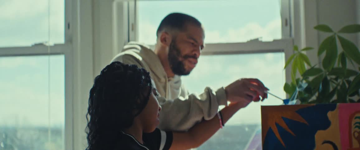 A father helps his daughter while painting picture in a sunlit room