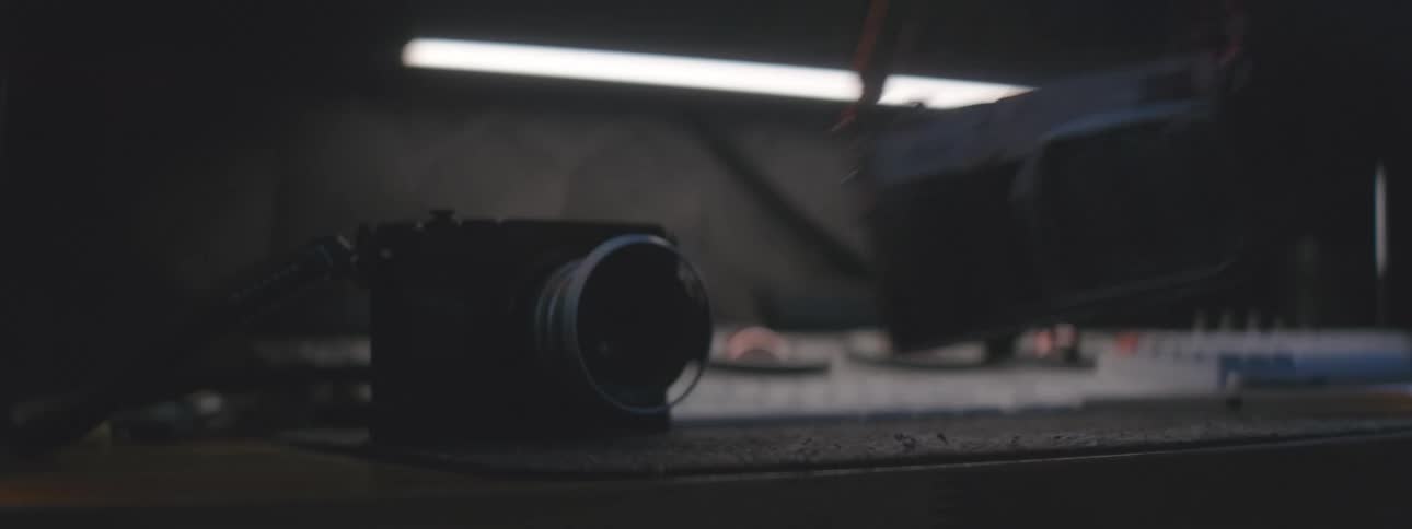 A pair of vintage cameras are being picked up from a dimly lit table with a fluorescent light fixture overhead