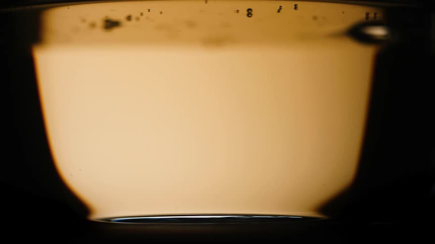 Light amber colored liquid pouring into a clear jar against a black background