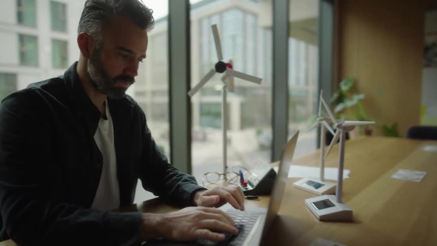 Man works on his laptop in a modern office with models of wind turbines on the table