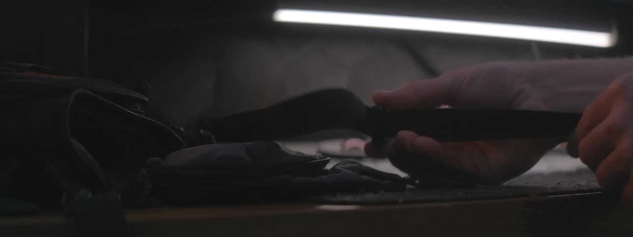 A persons hand tying a strap of a black backpack that is on a table