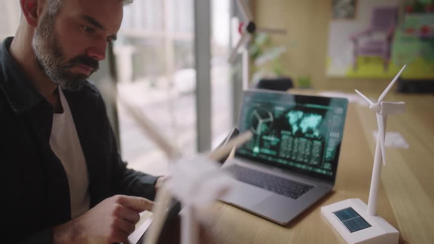 Man analyzes data on a tablet while working on a renewable energy project with wind turbine models