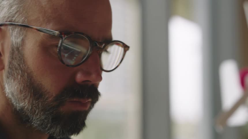 A bearded man with glasses types on a laptop in an office