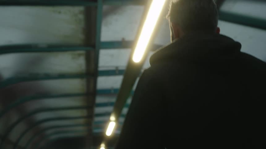 The back of a person with short gray hair wearing a dark hoodie walking through a covered walkway with a metal frame