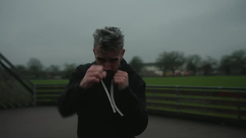 Man with focused expression practices boxing outdoors under a cloudy sky