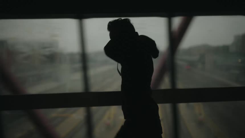 Man wearing a hood is jogging on a bridge over an urban city