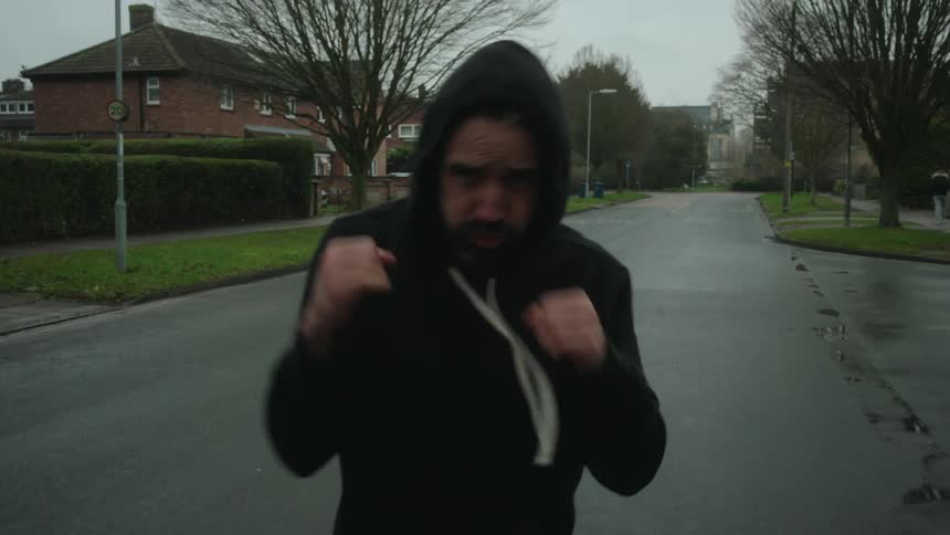 Man in cap outdoors in city with determined expression throwing boxing punches