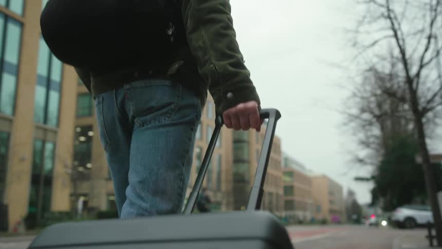 A person walking on a sidewalk and pulling a carryon backpack with wheels