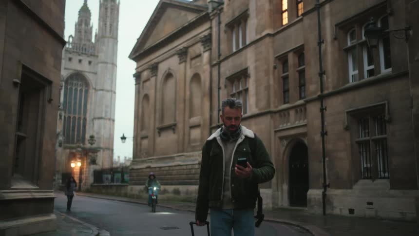 Man interacting with a smartphone walking through the streets of a classic city carrying a suitcase
