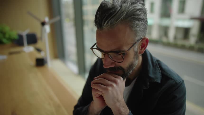 Man sitting at desk typing and looking thoughtful in front of a laptop