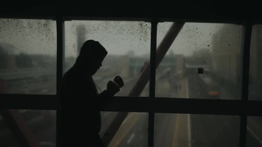 Silhouette of a hooded person appears on a glass walkway throwing boxing punches