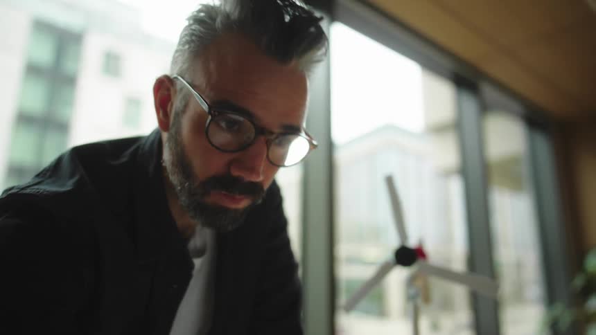 Man putting on glasses and looking closely at a model of a wind turbine in a bright modern office