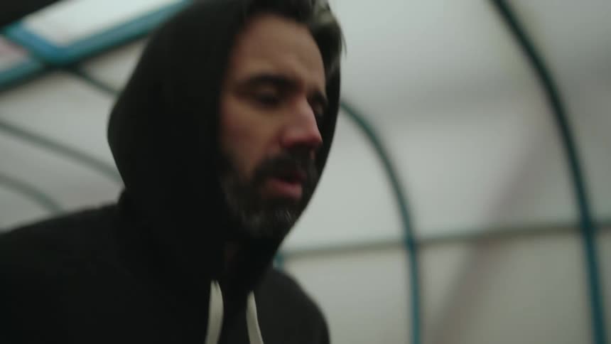 Hooded man runs under covered structure with determined expression
