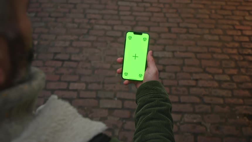 A man is walking on a cobblestone path while looking at his cell phone