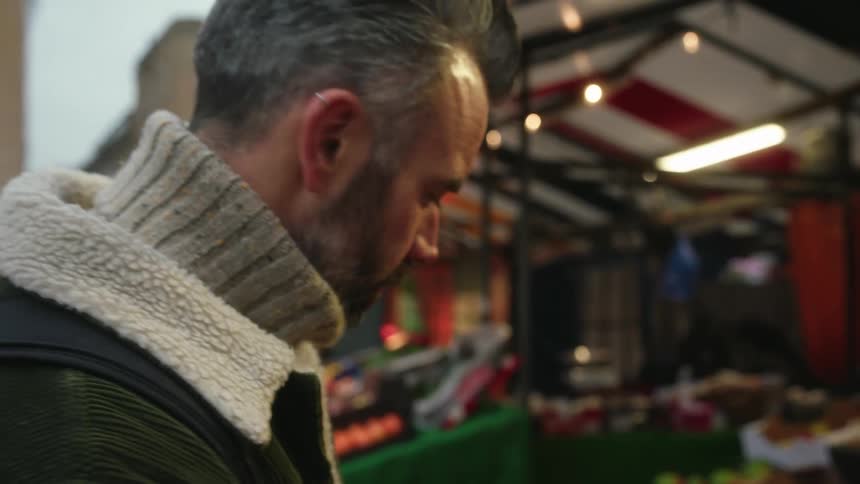 Man in wool coat smells a fresh tomato at an outdoor market