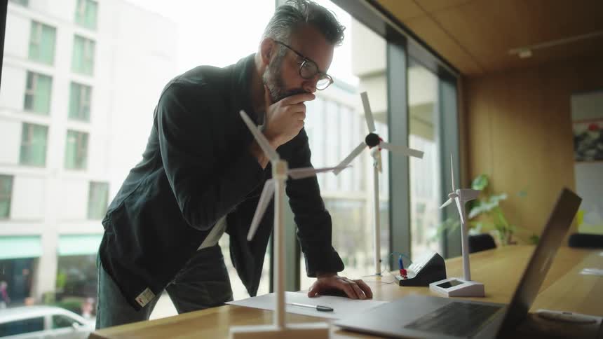 Thoughtful man standing in front of a laptop in an office room