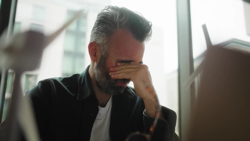 Portrait of a man sitting working and taking off his glasses tired
