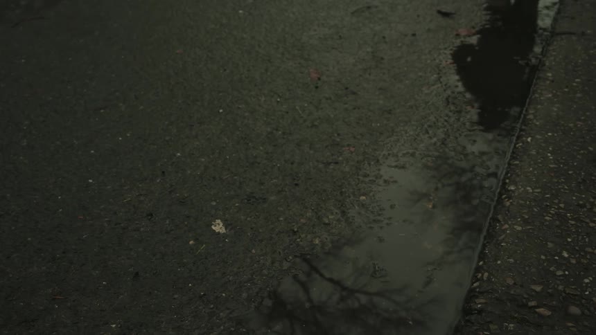 Person wearing white sneakers runs through a puddle of water on a wet sidewalk