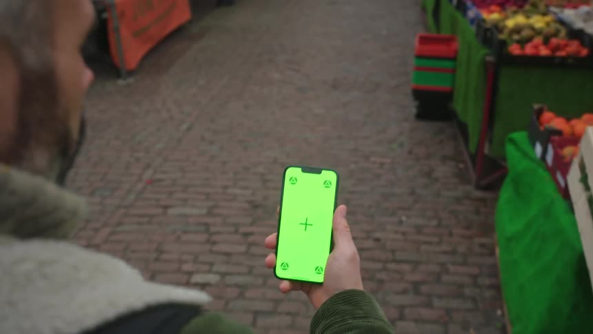 A person walking while holding a cell phone with a completely green screen