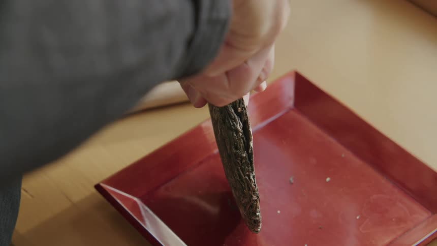 Person cuts a pressed tea disc on a red plate