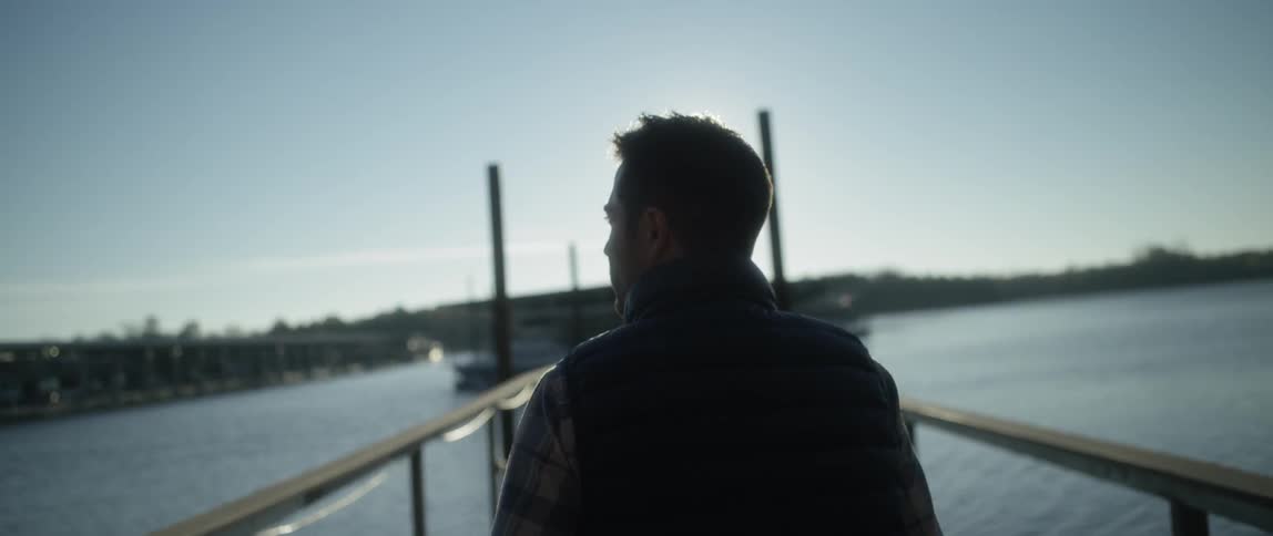The sun shines down on a man walking on a pier