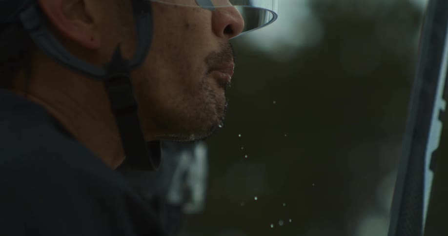 Man in helmet spits a jet of water while playing outdoor sports