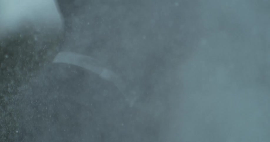 Ice particles spray through the air while a hockey player skates during an outdoor game