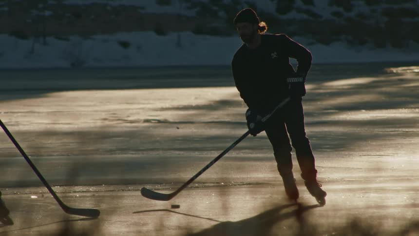 People in ice skates skating over a frozen lake playing hockey in the morning