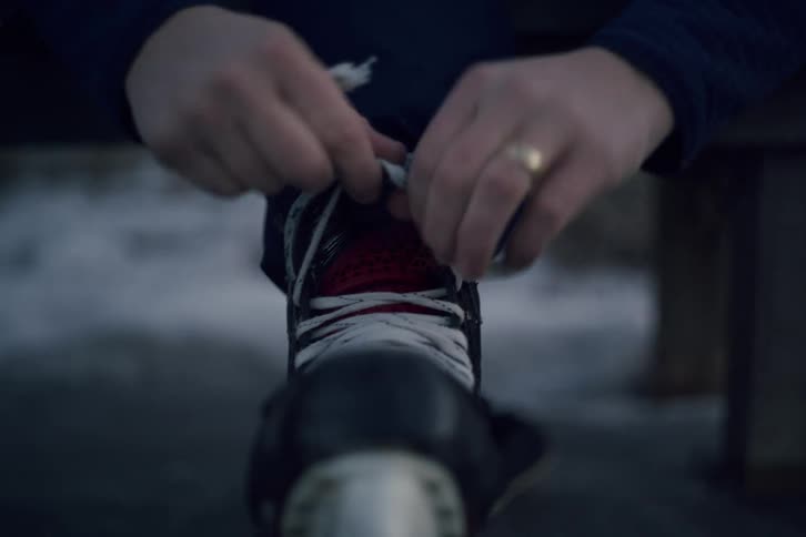 Man sitting on a bench on an outdoor ice rink laces his ice skates on a winter day