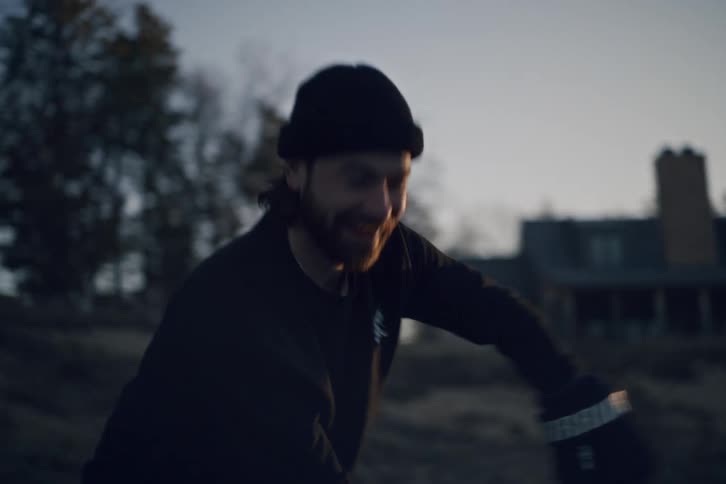 A man smiles while playing ice hockey with another adult on a frozen pond in a rural neighborhood