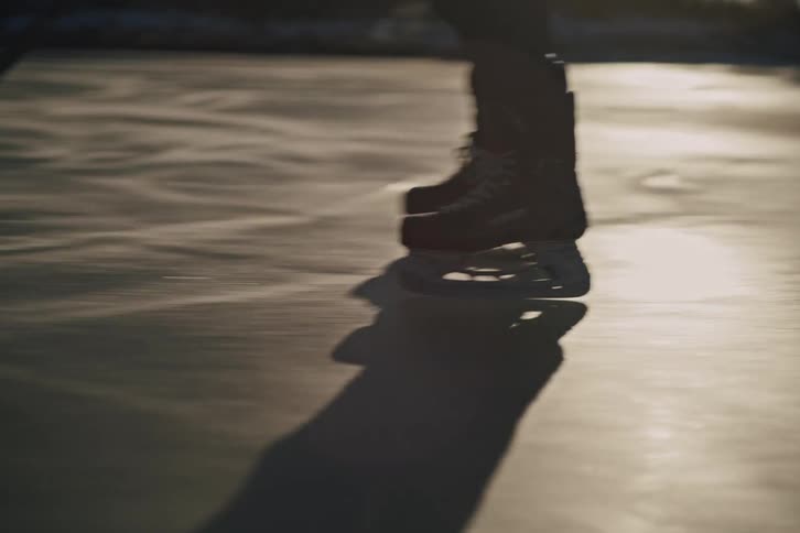 A persons ice skates and shadow as they glide across an ice rink