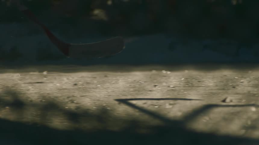 Hockey players glide across the ice as their sticks cast elongated shadows in the dusk