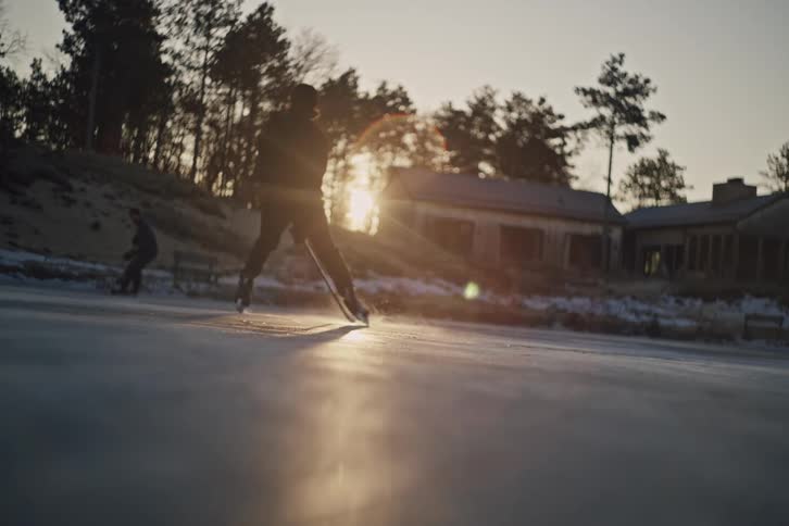 Two people playing hockey on an outdoor ice rink with the sun on the horizon