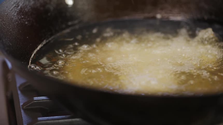 Hand placing a piece of food into hot oil to fry in a frying pan