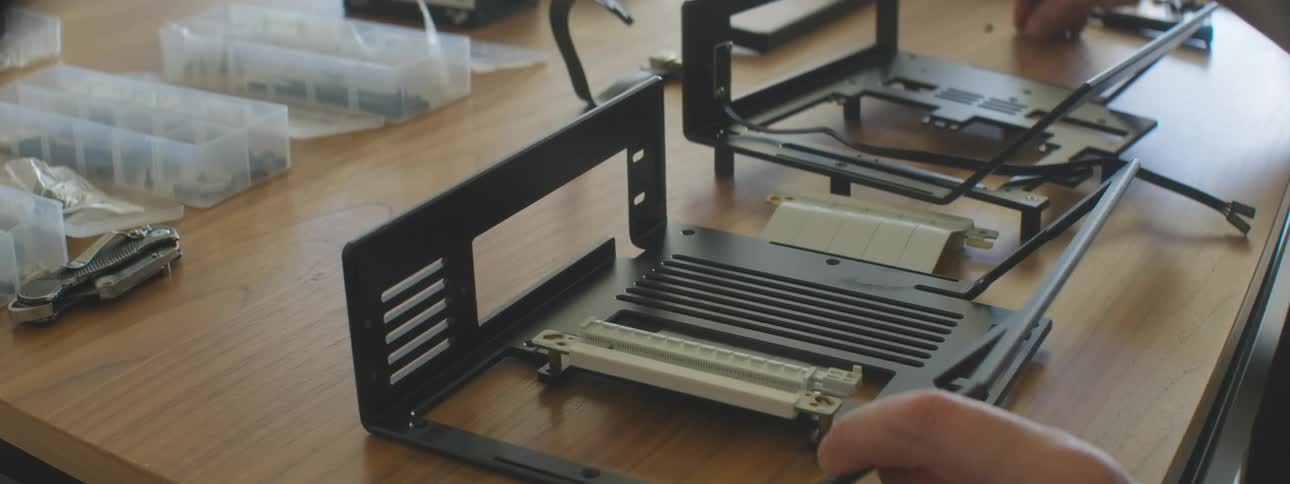 Hands assembling a computer case on a table with parts and tool organizers