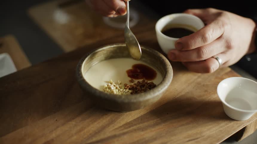 A person using a spoon to put brown sauce into a container of white food