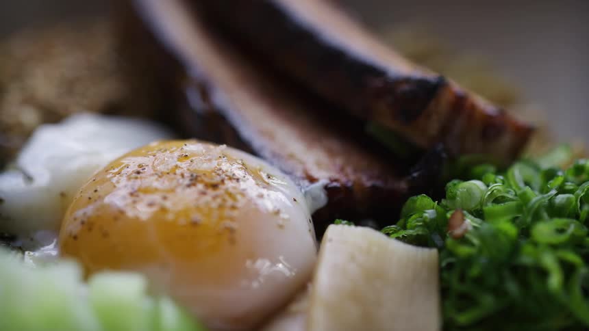 Poached egg seasoned with pepper next to vegetables and pieces of grilled meat
