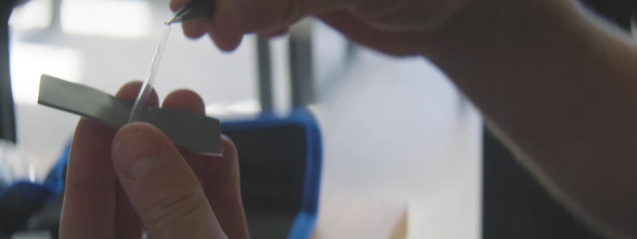 Pair of hands with tweezers removing a film from a component