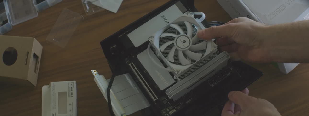 A hand is shown installing a motherboard with a white fan on a small computer frame