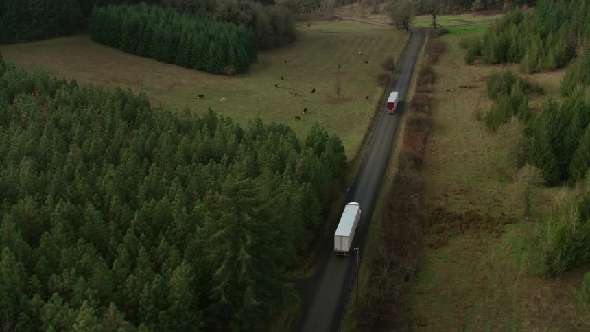 Aerial shot of two trucks traveling along a narrow road surrounded by vegetation