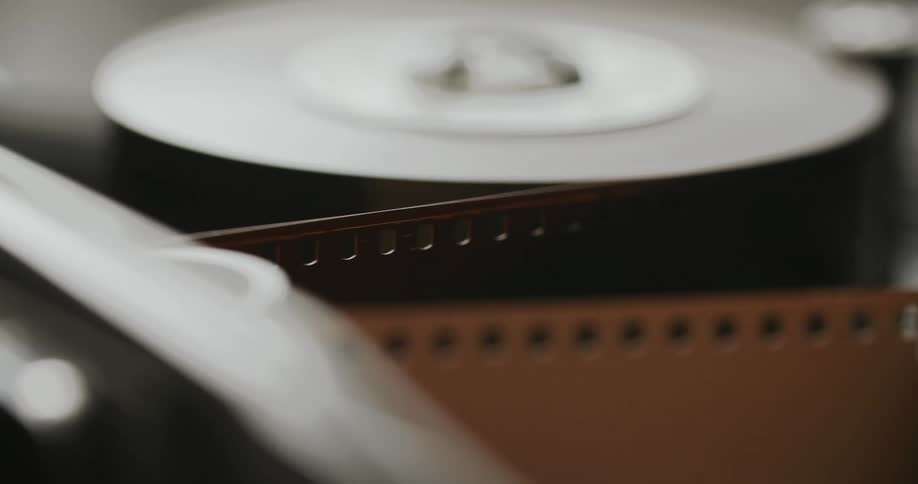 Closeup of a strip of film with perforations being processed through the reels of a machine
