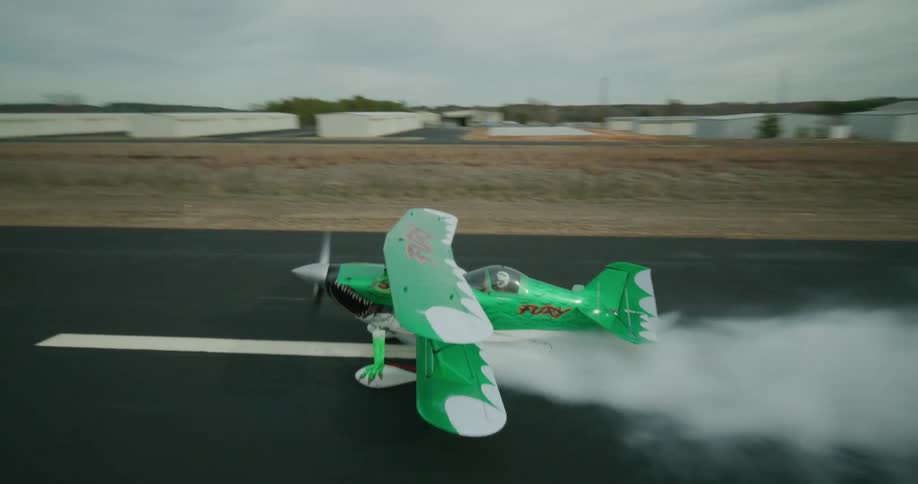 Small green aerobatic plane speeds down the runway leaving a trail of smoke