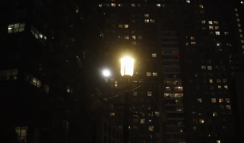 Streetlight illuminates the night amid tall buildings with lit windows
