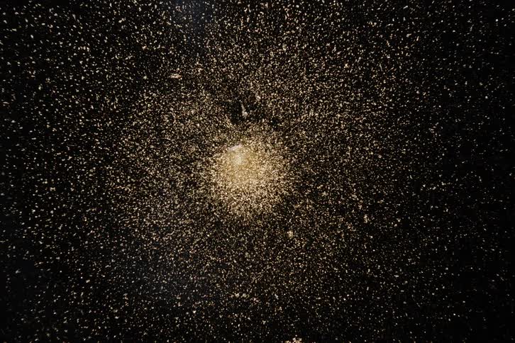 Nucleus exuding a golden dust against an abstract black background
