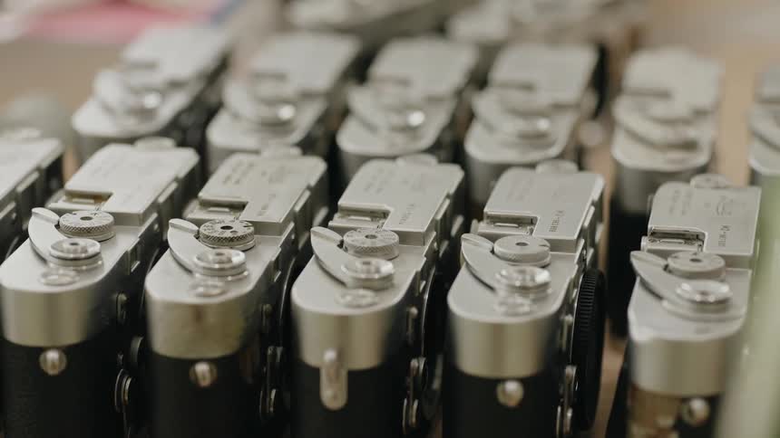 Multiple silver and black cameras are arranged in neat rows over a workbench