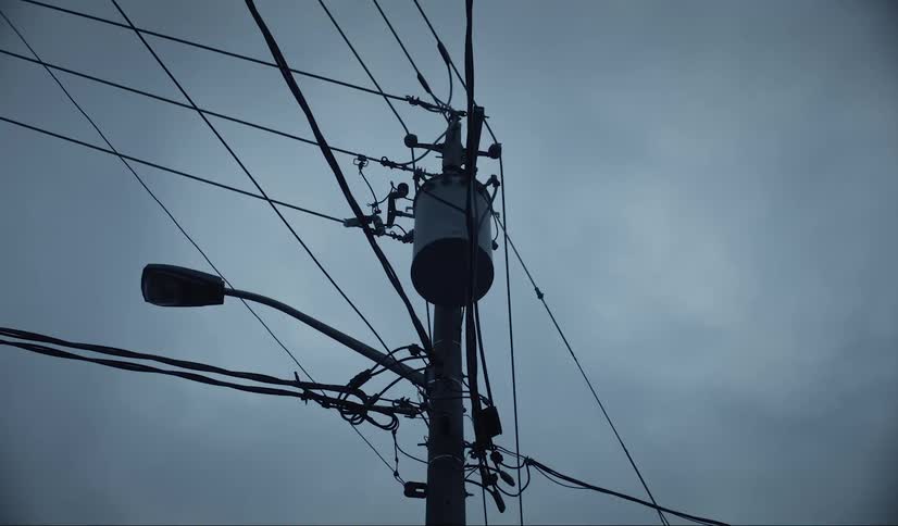 Upward view of a pole with power lines on a cloudy day